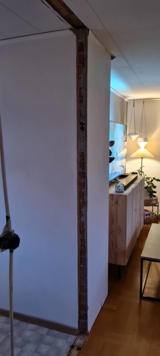 En delvis rivet vägg hörn som avslöjar tegelstenar i ett vardagsrum under renovering.