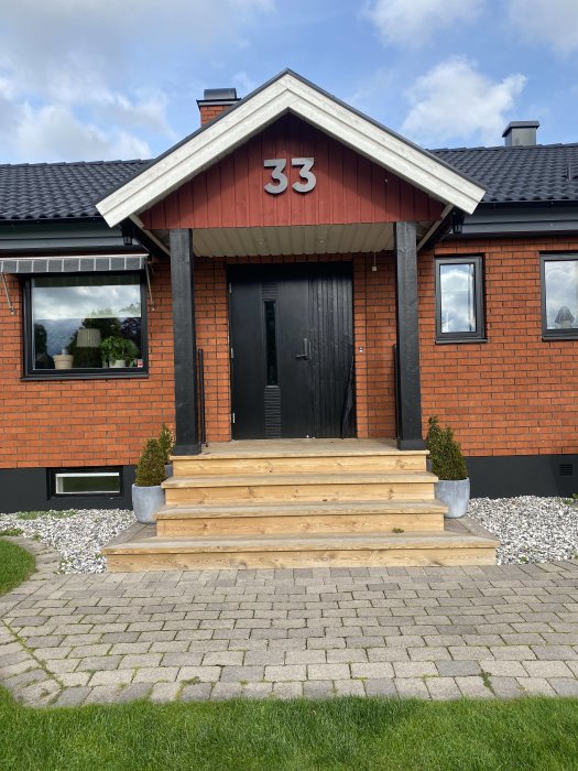 Husentré med nytt nummer "33" monterat på röd gavel, utan belysning, ovanför svart dörr.