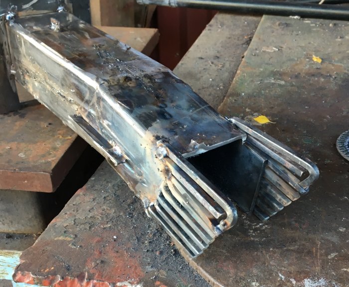 Svetsad metallprototyp av pelletsbrännare med zigzackmönster och anpassade sidor.