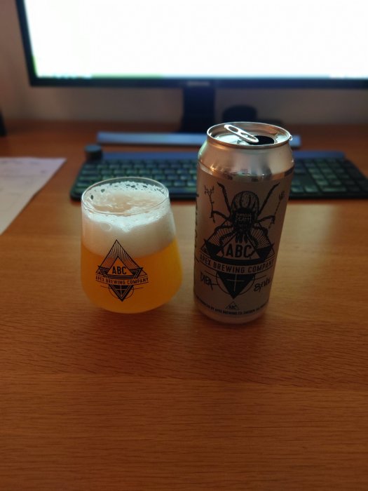 Apex-öl i glas bredvid en öppen burk på ett skrivbord med datortillbehör i bakgrunden.