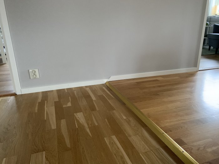 Hörnet av ett rum med snedkapad dörröppning och parkettgolv med vit list och dörrfoder.