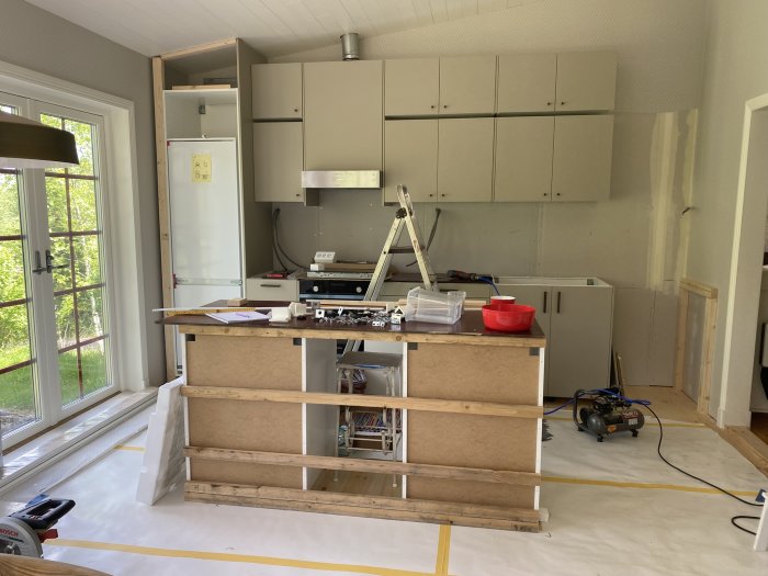 Pågående konstruktion av en köksö med träreglar, stommar och verktyg i ett kök under renovering.