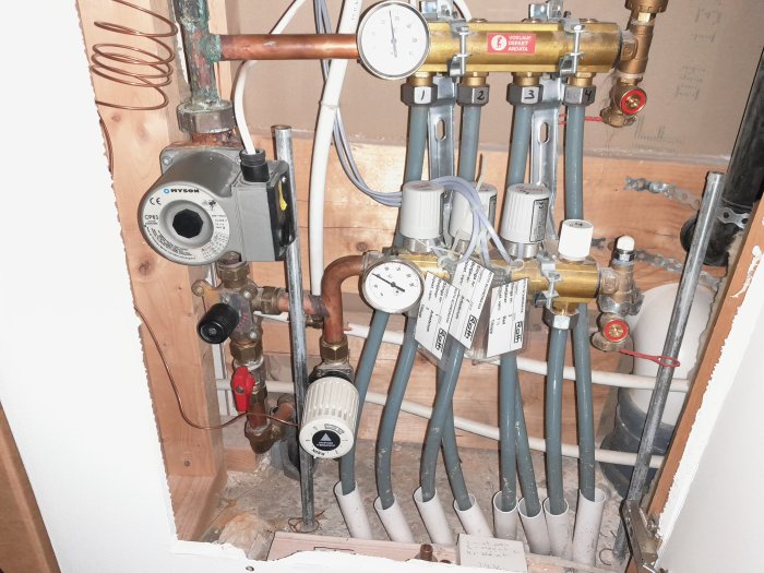 Värmesystem med kopparledningar, cirkulationspump och flervägsventiler i en väggöppning.