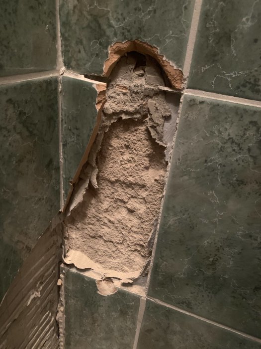 Skadad vägg med kakel som delvis är borttaget och exponerat underliggande murbruk.