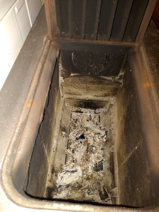 Insida av en smutsig och askfylld vedpanna i behov av rengöring.