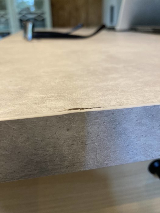 Närbild på en spricka längs kanten av en ljus laminatskiva som visar en delaminering eller skada.