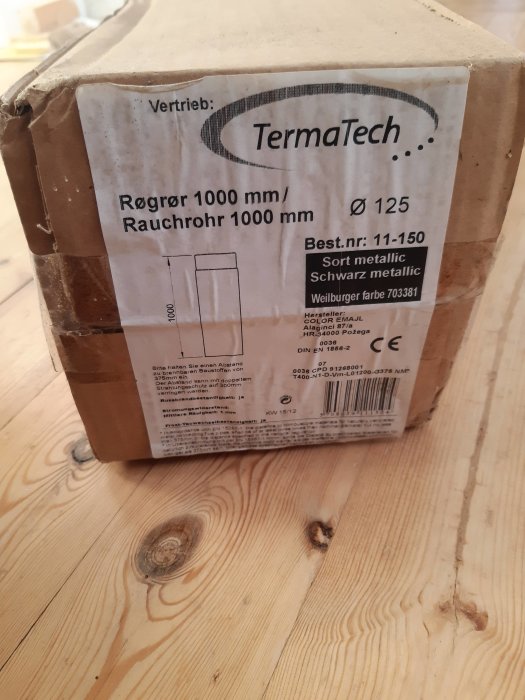 Sliten kartong från Termatech med text om rökrör på ett trägolv.