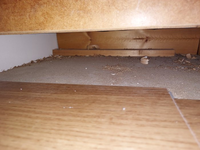 Sawdust and debris under kitchen cabinet during renovation.