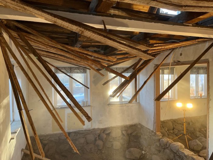 Renoveringsprojekt där träreglar och bjälkar i taket är delvis nedmonterade i ett rum under konstruktion.