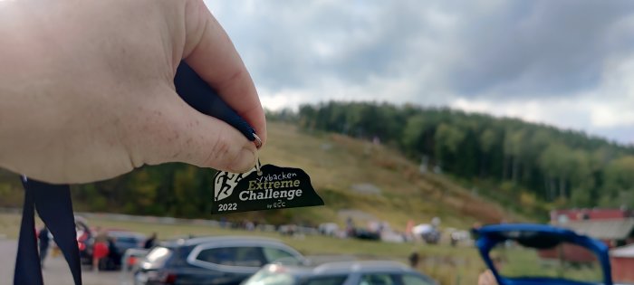 Hand håller en medalj från Ljusdalsbacken Extreme Challenge 2022, oskarp bakgrund av evenemang.