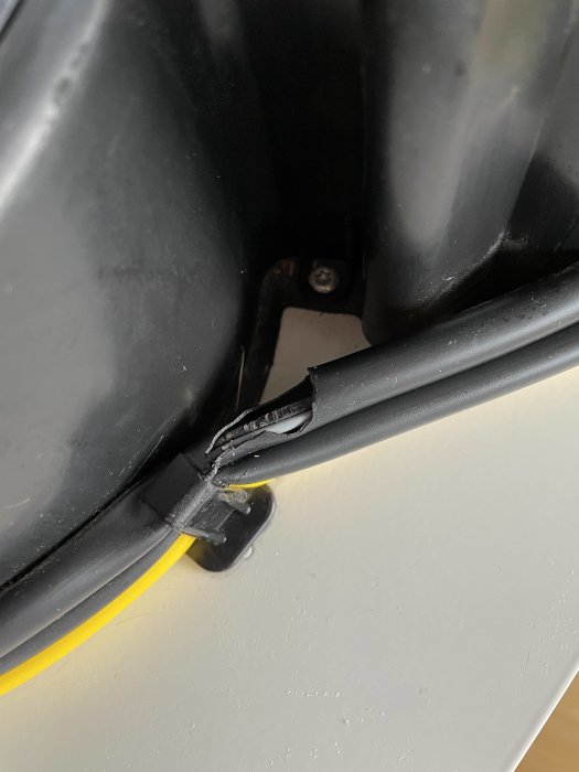 Trasigt svart plastskydd på apparat med gul kabel synlig, defekt som behöver åtgärdas.