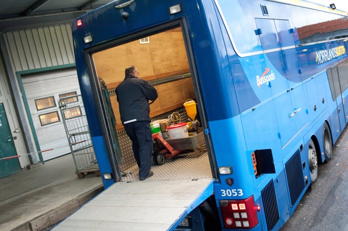 Arbetare lastar en handtruck med byggmaterial i ett busstransportfordon.