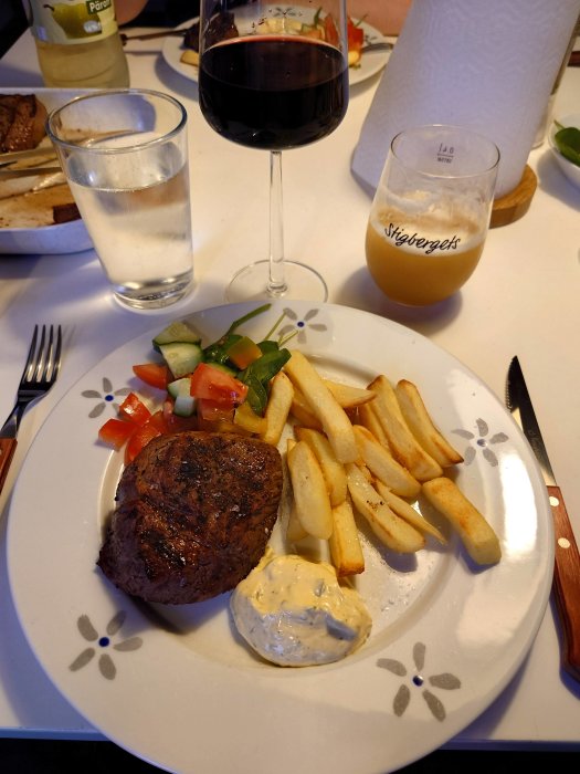 Grillad rostbiff med pommes, sås och sallad på en tallrik med ett glas vin och öl.