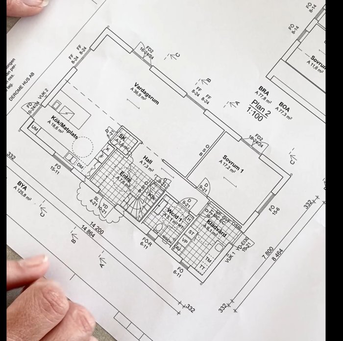 Ritad planlösning av ett hus med benämnda rum och mått, visas av person som håller i pappret.