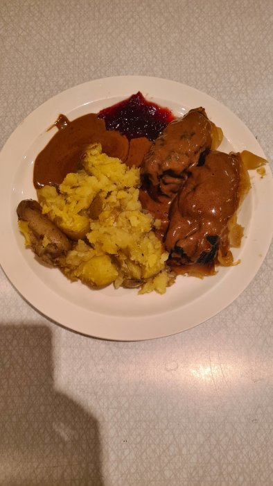 Hemlagade kåldolmar och krossad potatis med brun sås och lingonsylt på vit tallrik.