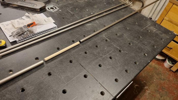 Metal curtain rods and a wooden dowel on a workbench, created to extend rod length for a custom fit.