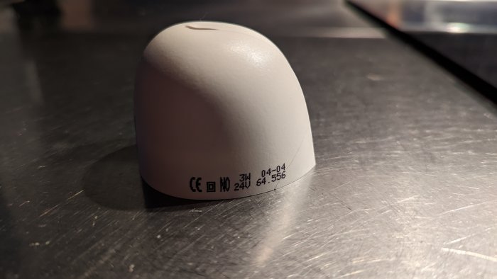 Plasthuv med synlig fördjupning och spricka, märkningar på sidan, på en blank yta.