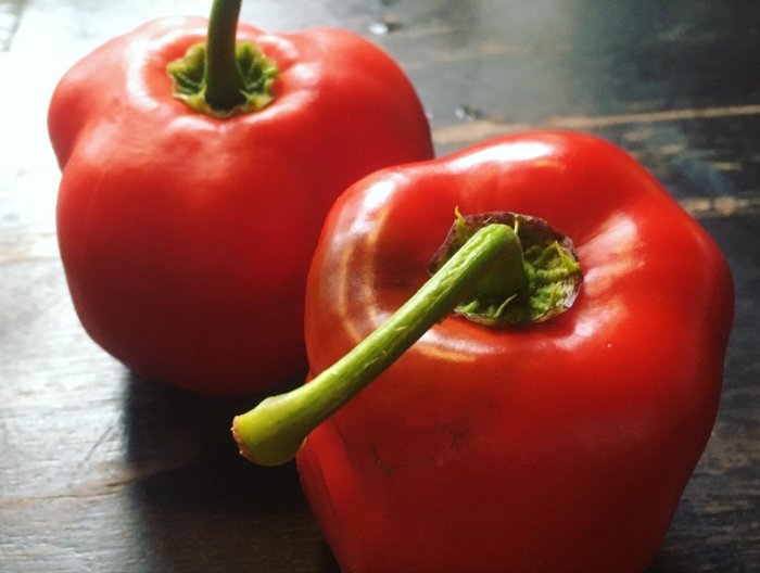 Två stora röda Rocoto Arequipa Giant-chilifrukter på ett mörkt träbord.