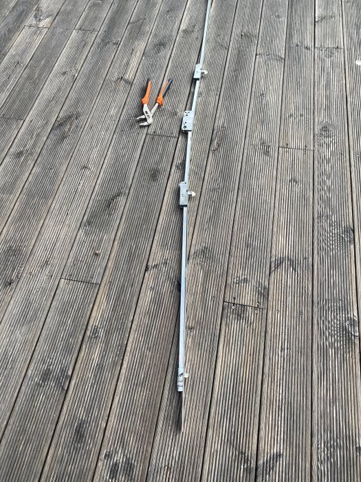 En demonterad spanjolett på ett trägolv bredvid två orange tänger.