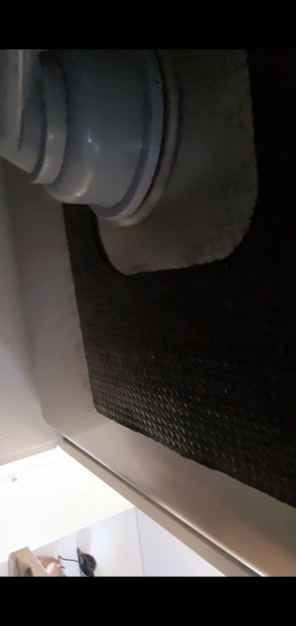 Flexibel ventilationskanal ansluten till tak med texturväv i förgrunden och delvis synlig inredning nedanför.