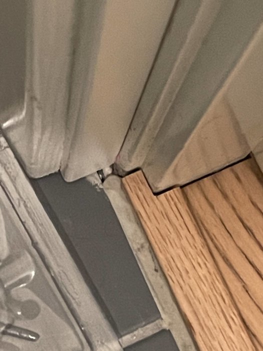 Närbild av en glipa där parkettgolv möter vägg och dörrfoder, med synlig ojämn skarv och tätning.