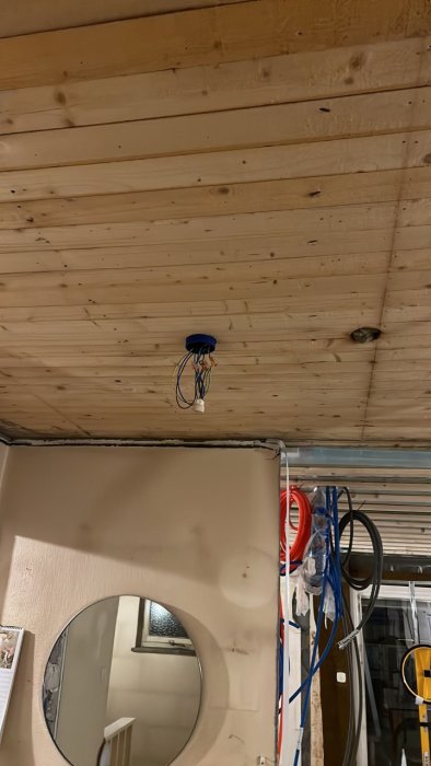 Nyinstallerad takdosa med elektriska kablar på ett trätak, ovanför en spegel och byggmaterial.