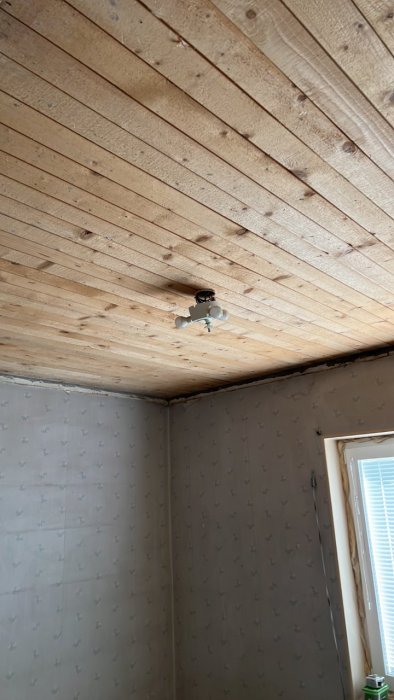 Nyinstallerad takdosa i ett rum med träpanel i taket och prydnadstapet på väggarna.
