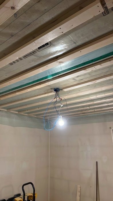Tillfällig belysning hängande från taket i underkonstruktion med synliga virkesreglar och isolering.