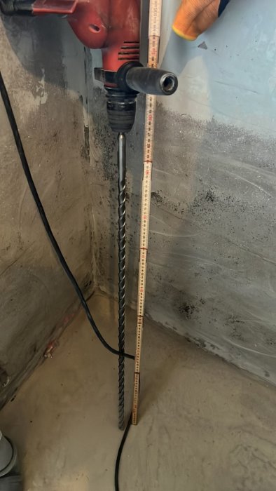 Lång 20mm betongborr insatt i borrhammare med mätlina bredvid på en dammig byggyta.