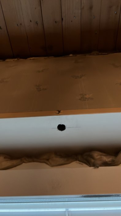 Vägg ovanför fönster med borrat hål för installation av spotlight, märkt med streck.