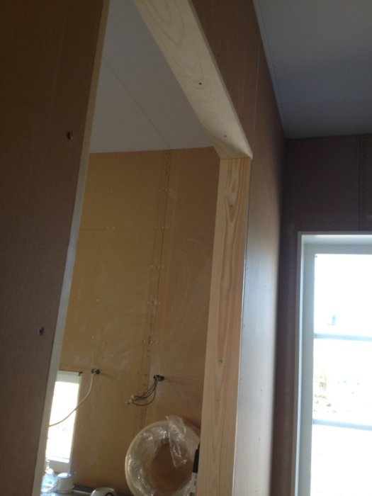 Halvfärdig vägginramning i ett byggprojekt, med oskyddade ledningar och plywood.