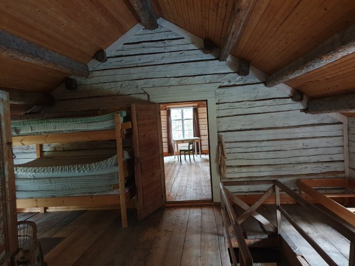 Interiör av rustik timmerstuga med våningssängar och trägolv.