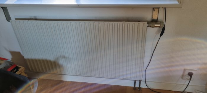 Ett traditionellt vitmålat radiator-element monterat under ett fönster, storlek 1200x650 mm, med termostat och elsladdar i närheten.