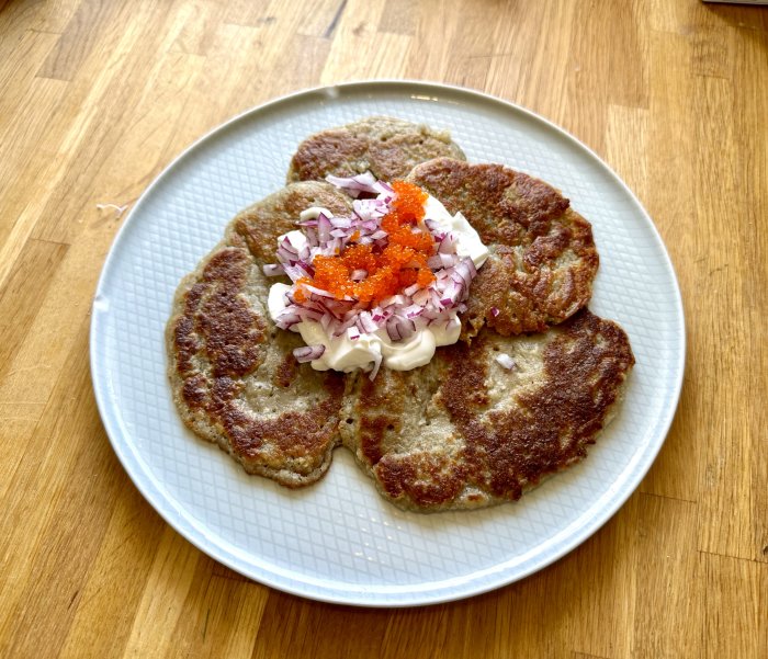 Solrospannkakor toppade med creme fraiche, hackad rödlök och tångcaviar serverade på en tallrik.