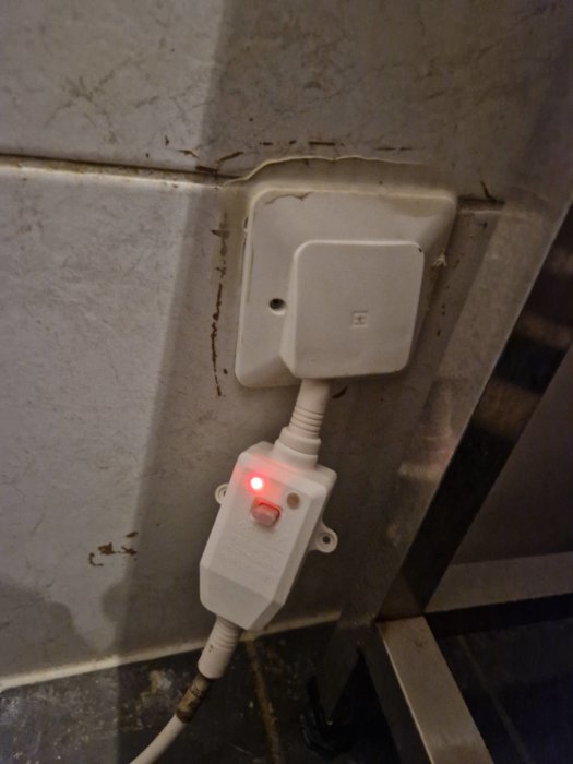 En strömbrytare med rött ljus och kabel som leder till en stängd eluttagsbox på en sprucken vägg.