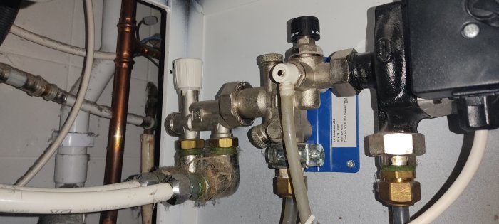 Rörsystem med ventiler och anslutningar mot en värmepump, synlig damm och spindelnät.