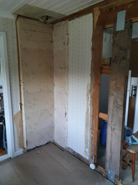 Delvis nedriven vägg med exponerade träreglar och gammalt tapetserat gipsskivor under renovering.