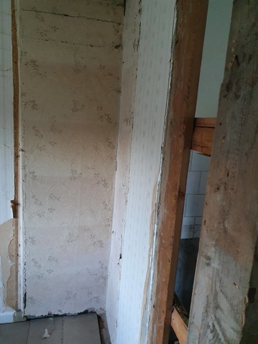 Renoveringsprojekt som visar gamla tapeter och trästommar i en orenoverad del av ett hus.