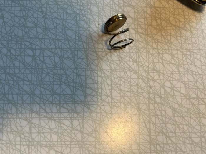 Glasbord med geometriskt mönster, metallfjäder och lösa föremål i dagsljus.