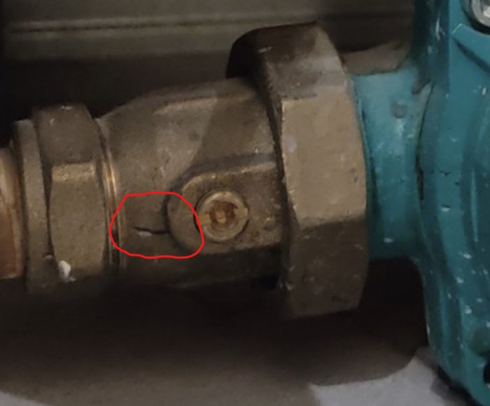 En närbild på en rörkoppling med en markerad spricka intill en blå pump, möjlig orsak till läckage.