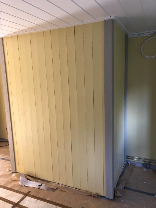 Nyinstallerad gul väggpanel i ett rum under renovering med synliga reglar och taklister.