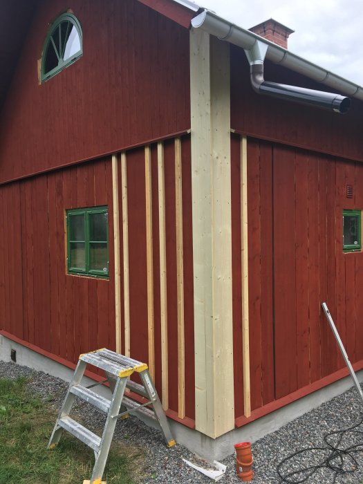 Rödmålad träfasad med ny lockläkt i olika bredder, stege, halvmånefönster med foder och hängränna vid takkanten.