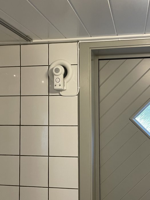 Luftvärmepump installerad ovanför ett fönster, med kaklade väggar och grå panel.