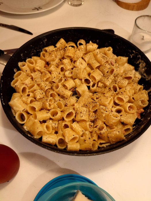 Stekpanna med krämig pasta och peppar, ett glas rött vin och rivet ost på sidan.