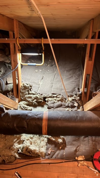 Öppen vindslucka som leder upp till en vindsutrymme med isoleringsmaterial och träreglar.