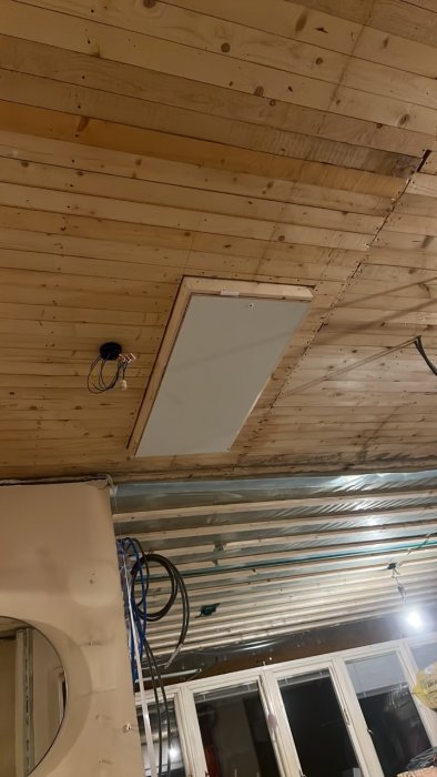Nyinstallerad vit vindslucka i ett tak med synlig råspont och elektriska installationer i förgrunden.