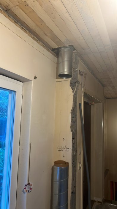 Renoveringsprojekt med en ventilationstrumma monterad i ett undertak nära en dörr.