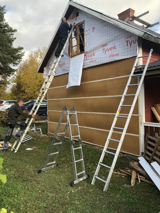 Två personer reparerar och isolerar västra gaveln på ett hus, omgivna av stegar.