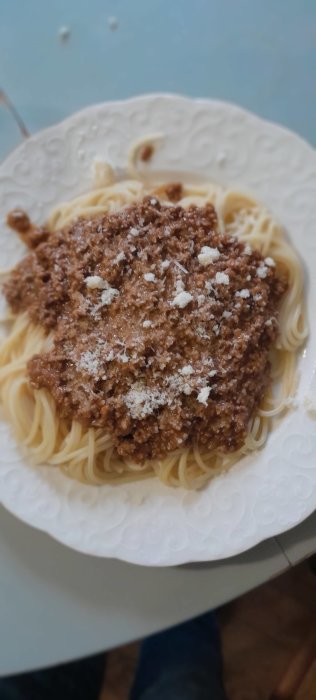 Tallrik med spaghetti bolognese toppad med riven parmesan, fotograferat ovanifrån.