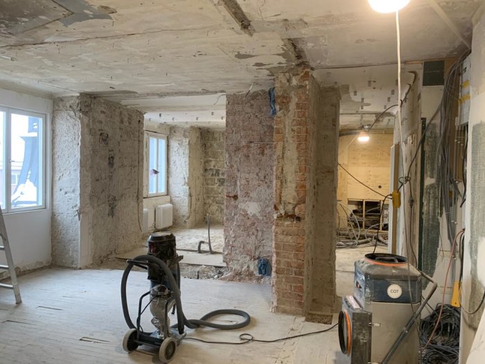 Bild på en lägenhets inre under rivningsfas, med exponerade tegelväggar, rör och avskalat tak.